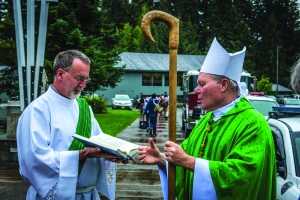 Deacon Mike Monagle assists Bishop Edward J. Burns as he blesses law enforcement and fire/rescue vehicles present at the annual Blue Mass on August 24 in Juneau honoring law enforcement and military personnel.  (Photo by Matthew S. Brown) 