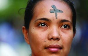 Woman with cross marked on forehead looks on during Ash Wednesday Mass outside church in Manila